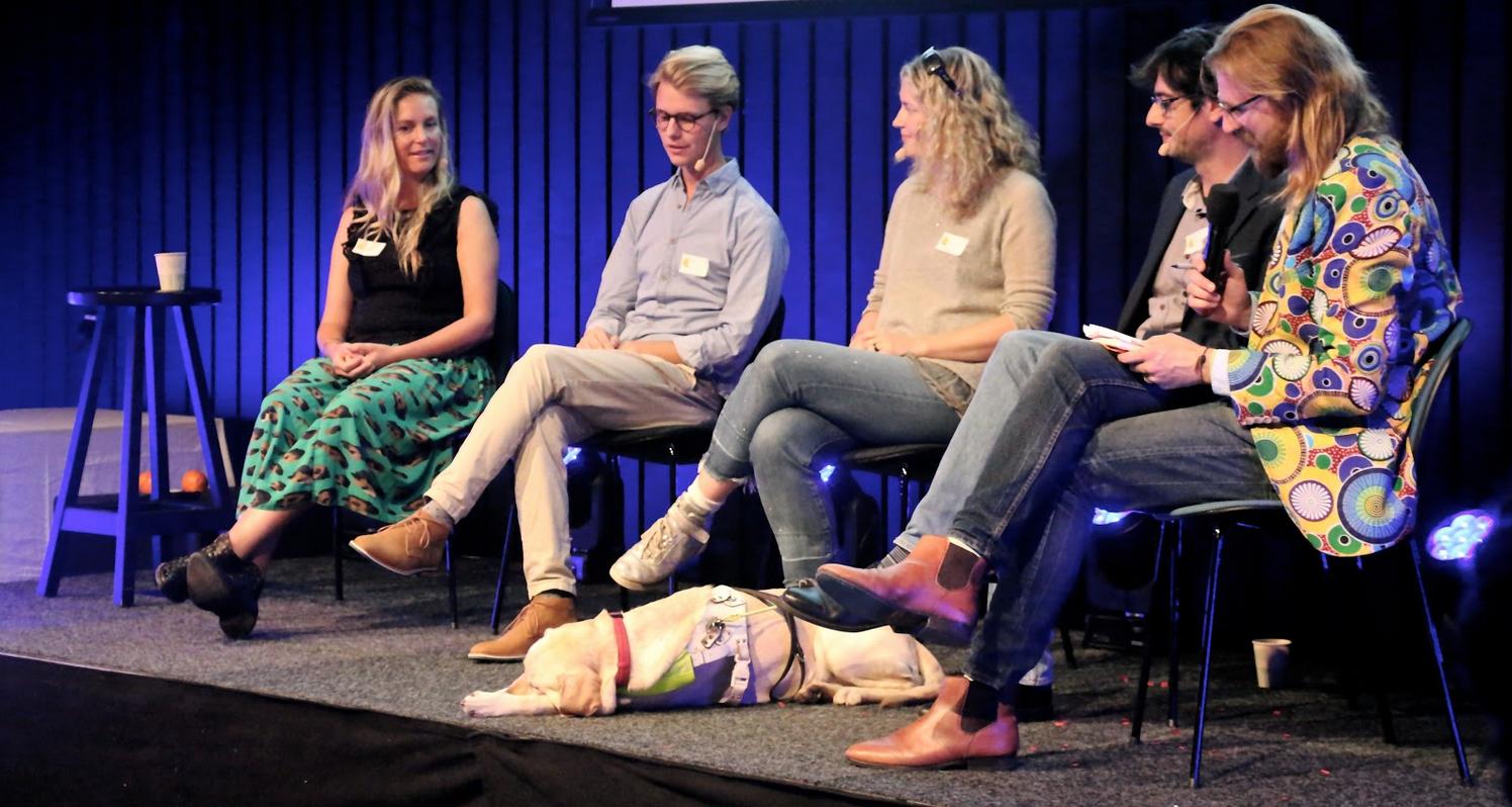 5 people on the panel. Anica sits in the middle with her sleeping guide dog near her feet. 